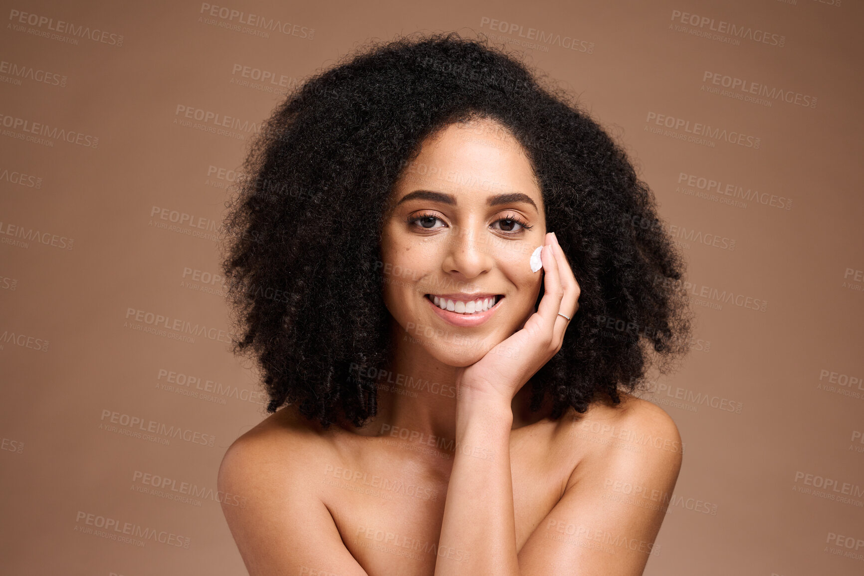 Buy stock photo Face, beauty and skincare with a model black woman in studio on a borwn background to apply lotion. Portrait, hand and hair with an attractive young female posing to promote a natural skin product