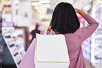 Woman, shopping and window display in a mall for retail. therapy, sale and customer discount at a store. Paper bag, fashion and female looking at clothes or makeup on promotion on commerce travel