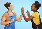 Interracial woman, friends and smile for high five, game or playing and standing isolated on a blue background. Happy women smiling and enjoying playful time together with hands for friendship