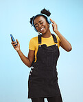 Black woman, phone and music in studio with smile, happiness or listening by blue background. Happy gen z girl, streaming audio or online radio on smartphone for edgy fashion, headphones and backdrop