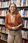 Education, student and woman in university library ready for learning. Face, portrait and happy female from Brazil standing by bookshelf with book for studying, knowledge and literature research.