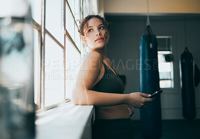 Buy stock photo Thinking, phone and fitness with a sports woman by a window, standing in the gym during an exercise workout. Health, idea and a female athlete using social media or an app to track her training