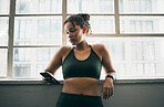 Idea, phone and exercise with a sports woman by a window, standing in the gym during a fitnesss workout. Health, thinking and a female athlete using social media or an app to track her training