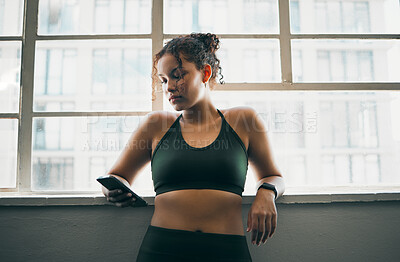 Buy stock photo Idea, phone and exercise with a sports woman by a window, standing in the gym during a fitnesss workout. Health, thinking and a female athlete using social media or an app to track her training