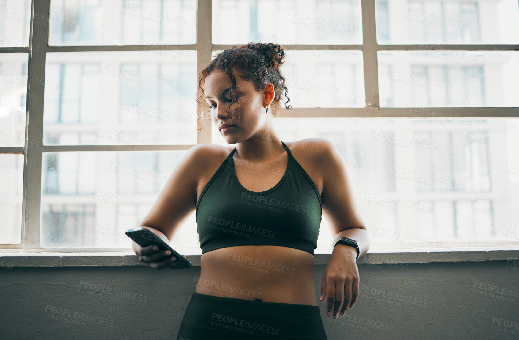 Buy stock photo Idea, phone and exercise with a sports woman by a window, standing in the gym during a fitnesss workout. Health, thinking and a female athlete using social media or an app to track her training