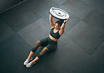 Fitness, weight plate and woman at gym for workout, exercise and training for health and body wellness. Strong sports female or bodybuilder on floor doing weightlifting for power, energy and balance
