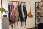 Clothes rack, apron and art with a broom in an empty workshop or studio against still life wall for design. Creative, pottery and clothing with a group of aprons hanging in a small business startup