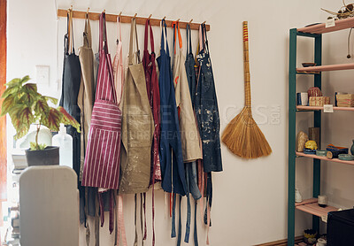 Buy stock photo Clothes rack, apron and paint with a broom in an empty workshop or studio against still life wall for design. Creative, art and clothing with a group of aprons hanging in a small business startup