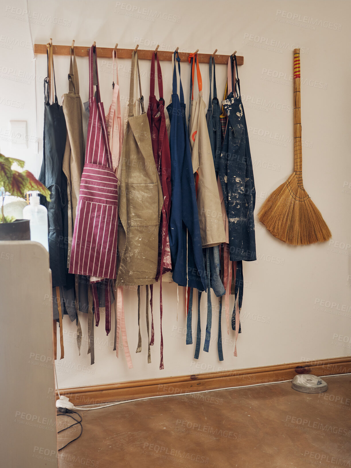 Buy stock photo Clothes rack, apron and pottery with a broom in an empty workshop or studio against still life wall for design. Creative, art and clothing with a group of aprons hanging in a small business startup