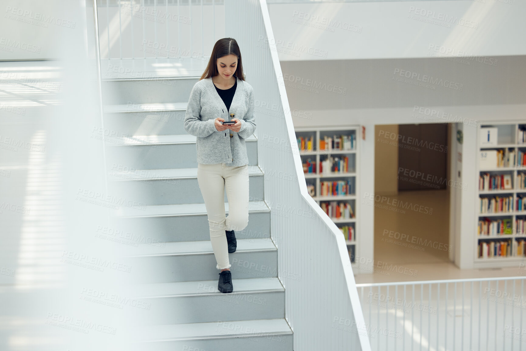 Buy stock photo Phone, social media and research with a woman in the library walking down stairs at university or college. Books, internet and mobile with a female student on a staircase in a bookstore for education