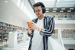 Phone music, headphones and student in library, university, or college research on mental health, wellness and education. Bookshelf, knowledge and creative, geek man listening to audio on mobile app