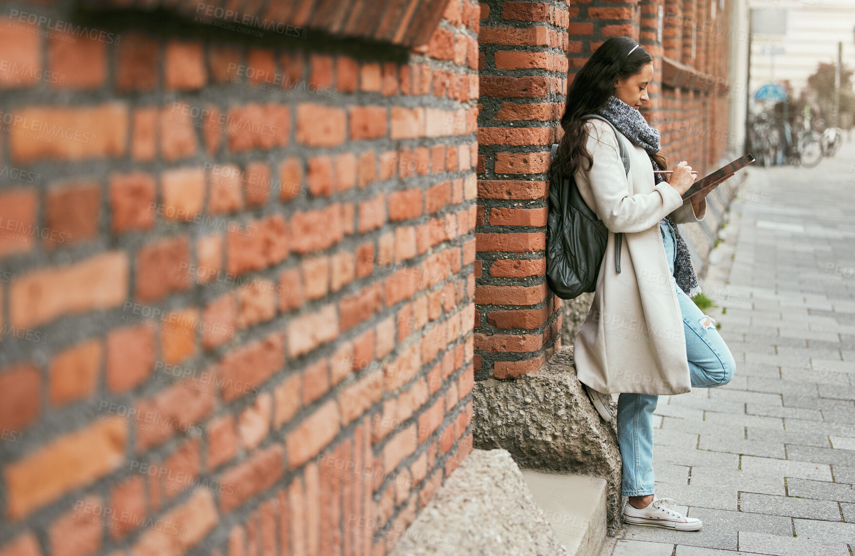 Buy stock photo Woman, student and tablet leaning on brick wall writing, design or doing research in the city. Female university learner or designer working on touchscreen with wireless pen or tech in a urban town