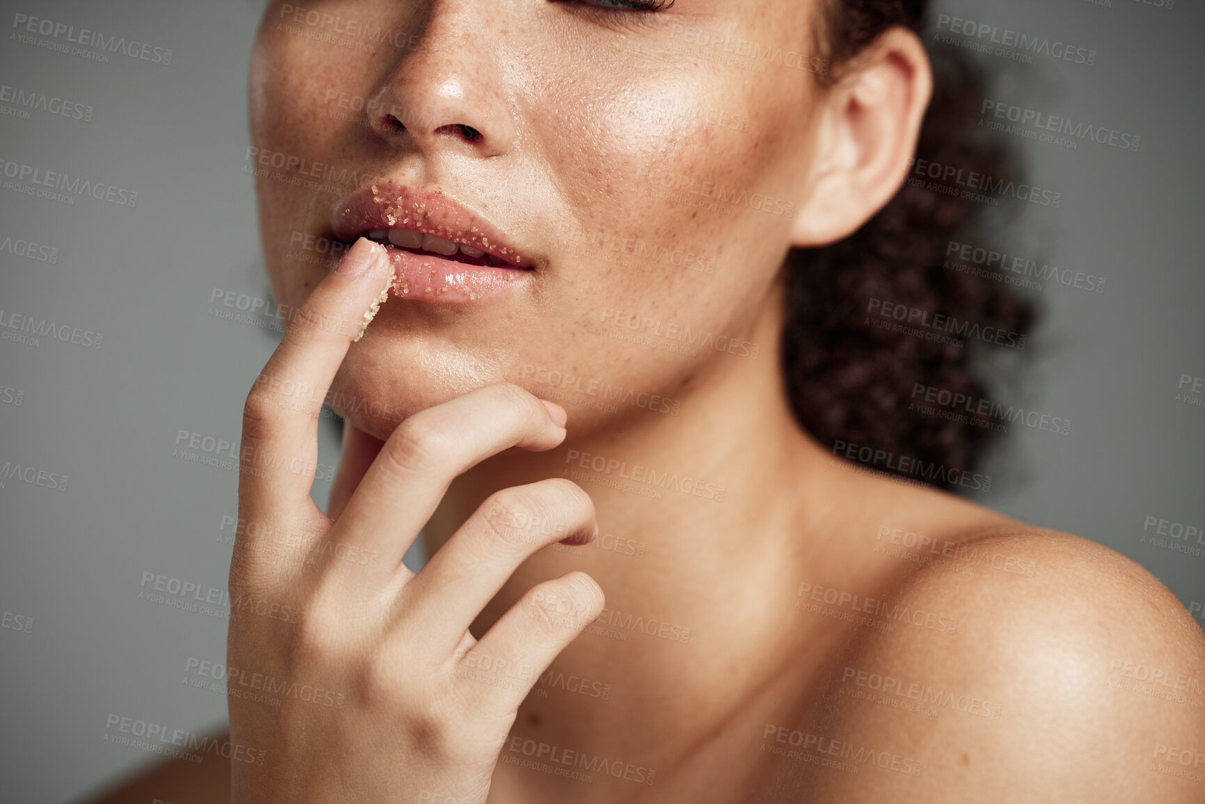 Buy stock photo Woman, hand and lips in sugar scrub for skincare, makeup or cosmetics against a grey studio background. Happy female applying treatment for facial cosmetic, lip dermatology or mouth exfoliation