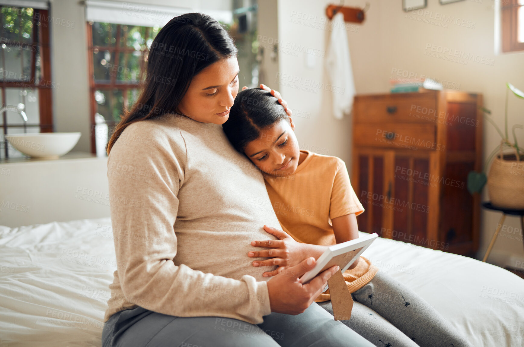 Buy stock photo Pregnant mom and child look at a picture frame together in the bedroom of their modern house. Sad, emotional and mother with pregnancy holding her girl kid while looking at a photo on the bed at home