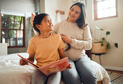 Buy stock photo Family, book or learning and a girl reading in a bedroom with her mom playing with her hair in their home. Books, education and love with a mother and daughter bonding while sitting on a bed together