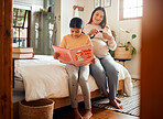 Family, books or education and a girl reading in a bedroom with her mom playing with her hair in their home. Book, learning and love with a mother and daughter bonding while sitting on a bed together