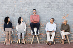 Creative business people, waiting room and man standing out against a brick wall for interview, meeting or opportunity. Group of employee interns with technology looking at candidate for startup