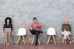 Business people, waiting room and sitting on chairs against brick wall for interview, meeting or opportunity. Group of creative interns in social distancing, working and checking time for startup