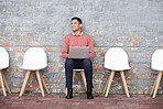 Recruitment, thinking and man on brick wall sitting in line with laptop for job opportunity, hr email and success. Computer, waiting room and person on Human Resources website for career application