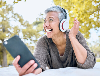 Buy stock photo Music, headphones and senior woman with phone at park streaming radio or podcast. Thinking, cellphone and happy, elderly and female in retirement enjoying audio while laughing at comic meme.