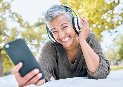 Buy stock photo Headphones, music and old woman with phone at park streaming radio or podcast. Social media, cellphone and happy, elderly and retired female with mobile, laughing at funny meme and enjoying audio.