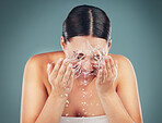 Woman face, water splash and washing for skincare, beauty and dermatology on a studio background. Health and wellness of a aesthetic beauty model person cleaning skin or body for facial spa treatment