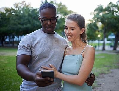 Buy stock photo Love, phone or couple of friends in a park on social media or relaxing on a romantic date in nature at sunset. Interracial, black man and happy woman enjoying online content on a fun holiday vacation