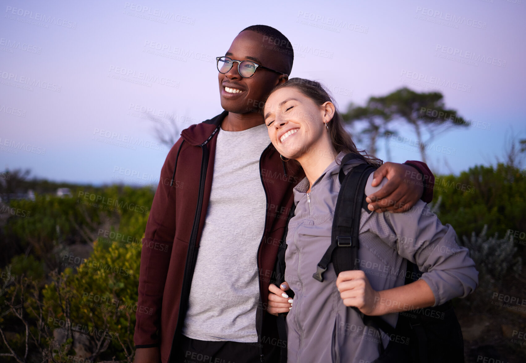 Buy stock photo Couple, adventure and interracial relationship during sunset in the evening or night outdoors in nature. Love, travel and people hugging outdoors after hiking a mountain and are happy and smiling