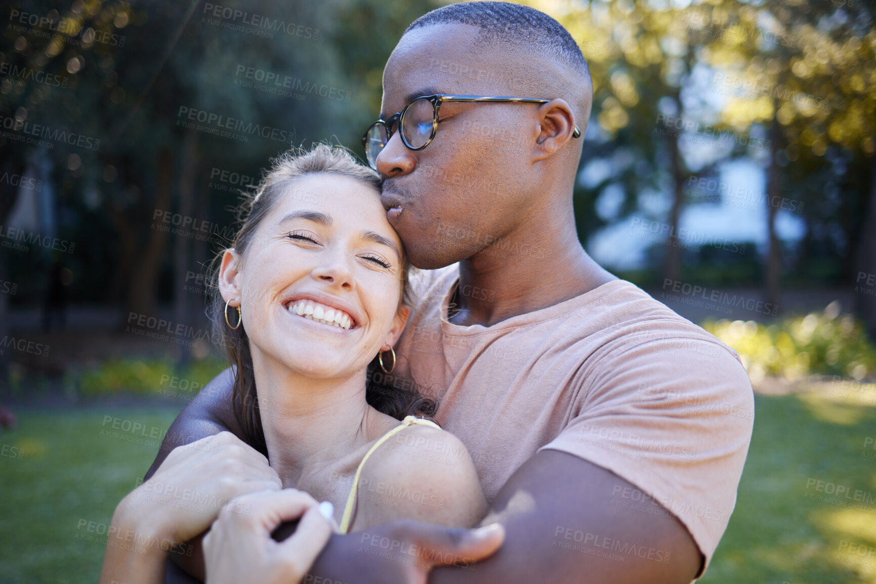 Buy stock photo Interracial, couple hug and kiss in park, date outdoor in nature, happiness with love and commitment in relationship. Trust, support and happy woman with smile, black man content with fresh air