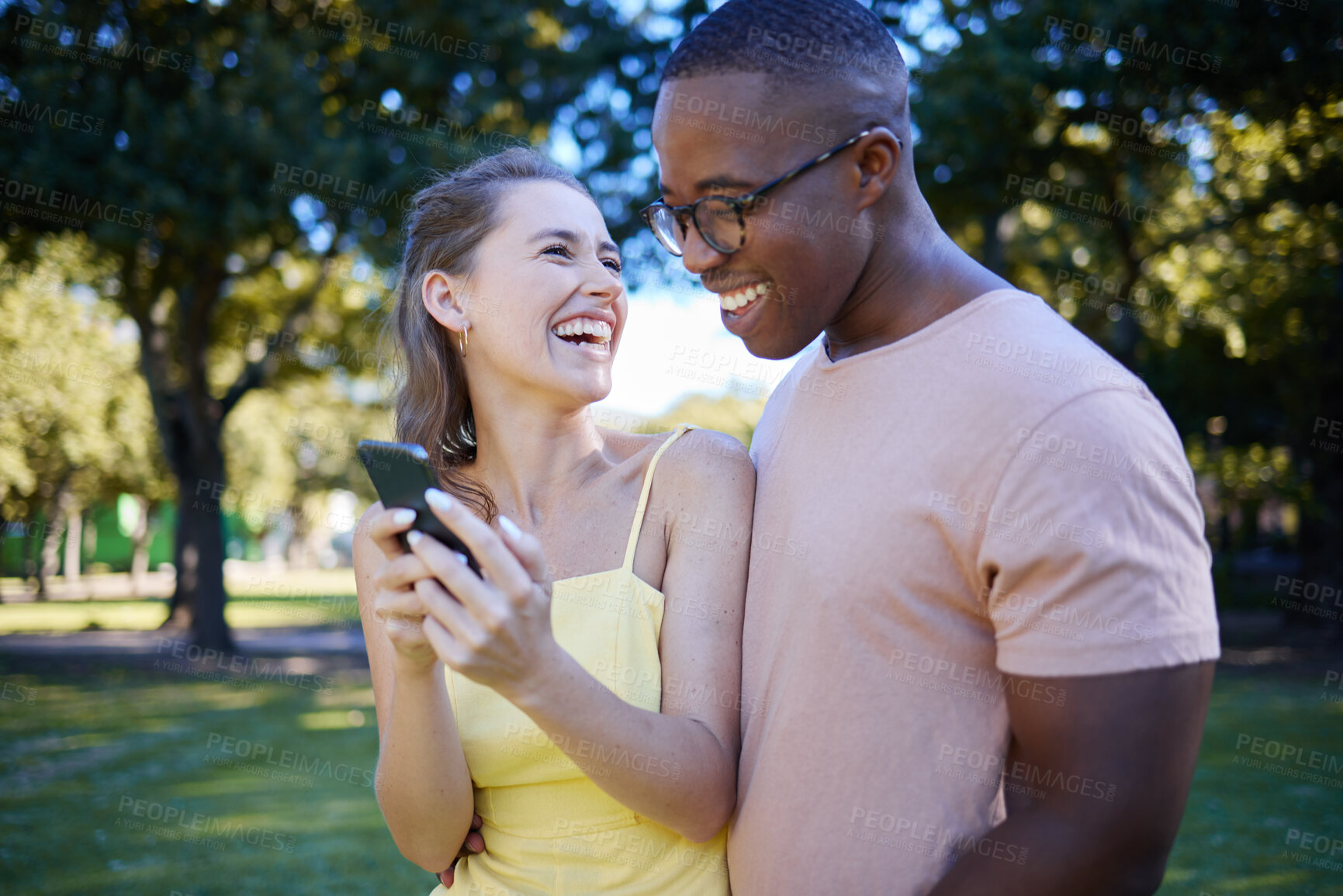 Buy stock photo Interracial, social media and couple with a phone in nature, funny communication and laughing at meme. Comic, streaming and black man and woman reading a joke on a mobile in a park in France