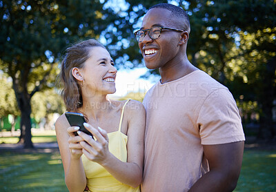 Buy stock photo Comedy, laughing and interracial couple with a phone in nature, funny communication and smile at a meme. Comic, streaming and black man and woman reading a joke on a mobile in a park in France