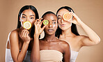Skincare, diversity and women with fruit, cosmetics and dermatology with friends on brown studio background. Face, vitamin c or ladies with natural beauty, girls and nutrition with healthy lifestyle 