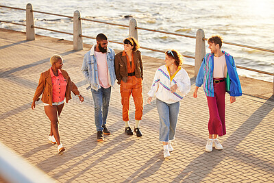 Buy stock photo Diversity, friends and walking seaside, talking and break in summer holiday, bonding and conversation. Multiracial, men and women on promenade, discussion and vacation with sunshine or relax together
