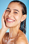 Face portrait, skincare shower and woman in studio isolated on a blue background. Water splash, beauty and happy female feeling fresh after bathing, cleaning and washing for healthy skin and wellness