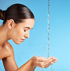 Woman, hands and water for face wash, skincare hydration or hygiene against a blue background. Beautiful female model in facial cleaning, washing or cleansing for skin rehydration or dermatology