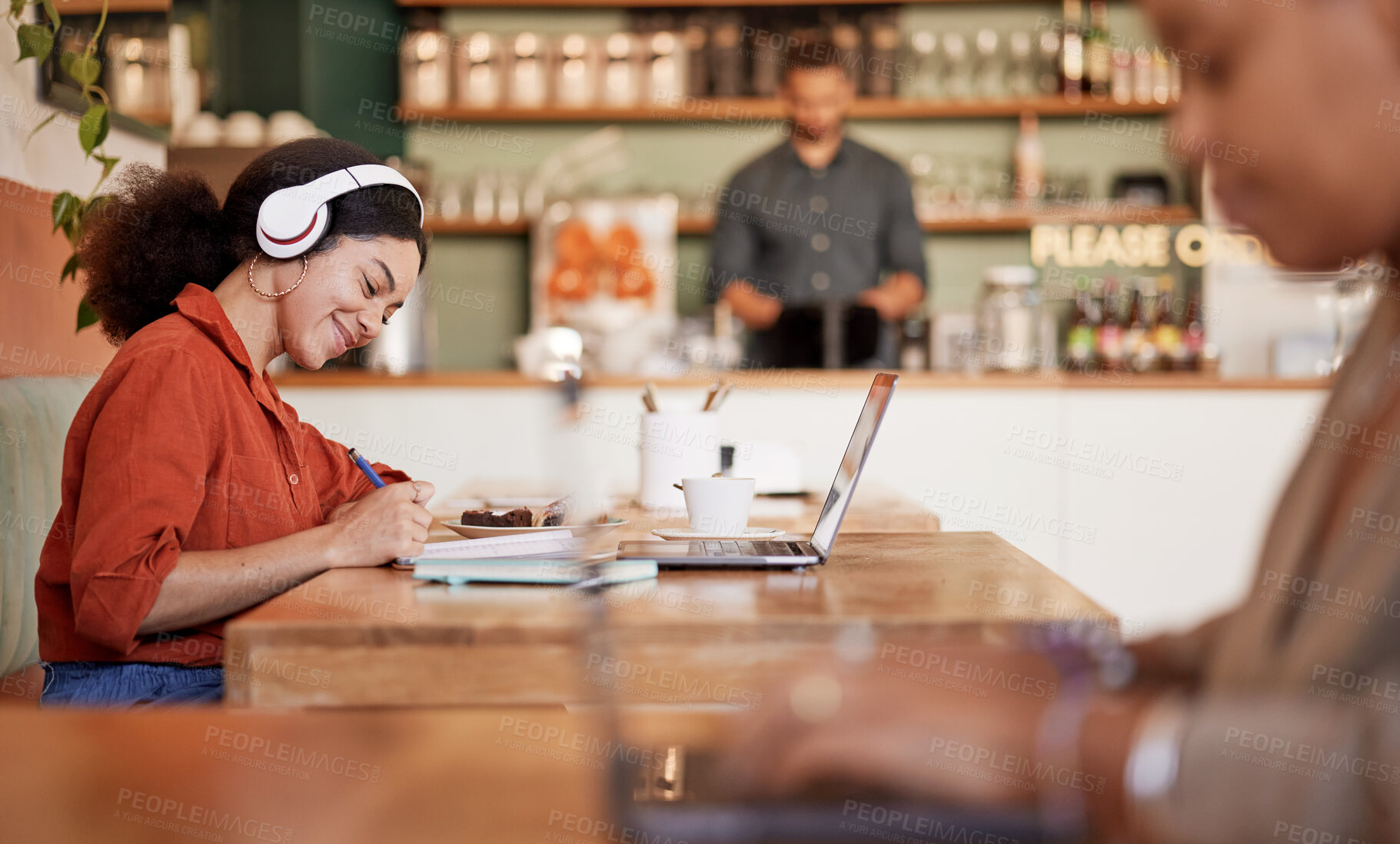 Buy stock photo Woman, student and studying in cafe, laptop and make notes for exams, smile and concentration for test. Young female, lady or academic with headphones, podcast or writing audio to text in coffee shop