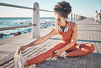 Black woman, seaside and stretching for workout, training and exercise for wellness, energy and health. African American female, girl and athlete stretch legs, promenade and fitness for stress relief