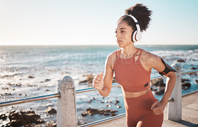 Buy stock photo Black woman, fitness and running with headphones at the beach on sea point in Cape Town for exercise. Sporty African American female runner by the ocean coast having a run for cardio training workout