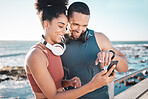 Fitness, couple and phone with smile for social media, communication or discussion relaxing by the beach. Happy man and woman smiling in happiness looking or browsing on smartphone by the ocean coast