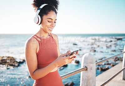 Buy stock photo Black woman at beach, headphone and phone with fitness, runner listening to music for sports motivation. Happy, streaming online with podcast or radio, smartphone and running by sea with calm outdoor