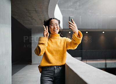 Buy stock photo Woman, peace and selfie in office building, smile and happy while on internet, pose and emoji. Asian, girl and business entrepreneur with smartphone for photo, peace sign and hand for profile picture