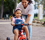 Mother, child and bicycle teaching with training wheels for learning, practice or safety at the park. Happy mom helping little girl to ride a bike with smile for proud playful moments in the outdoors