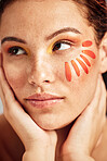Face, makeup and flower petal on skin of a woman for dermatology and cosmetics. Facial, wellness and self care for freckles glow, floral product and creative orange color on a healthy model in studio