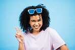 Portrait, black woman and sign for peace, fashion and casual outfit with girl on blue studio background. African American female, confident lady or gesture with sunglasses,  happiness and on backdrop