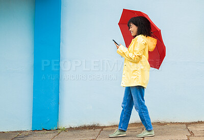 Buy stock photo Woman, raincoat and phone typing with umbrella on city street for social media, internet or urban communication. Smile, happy and walking student with mobile technology for weather app check for rain