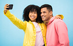 Happy couple, bonding and phone selfie on isolated blue background for social media, profile picture and travel vlog. Smile, happy man and black woman on mobile photography technology in Brazil city