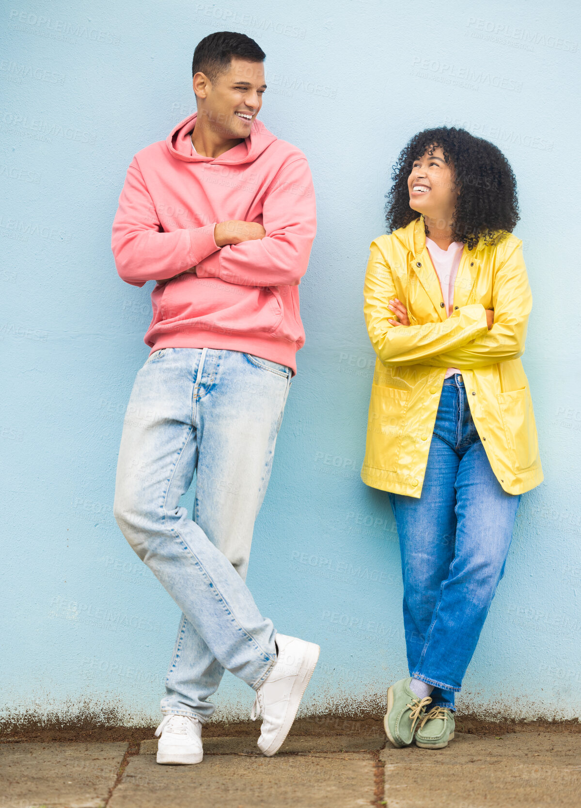 Buy stock photo Happy couple, smile and cool fashion standing in urban town wall background for conversation, peace and relax together. Casual man, trendy woman and happiness speaking for millennial street style 