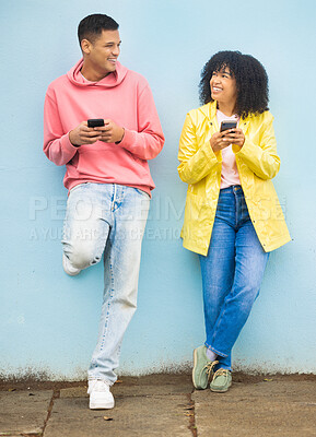 Buy stock photo Happy friends, phone and smile leaning on a wall enjoying social media, conversation or communication in the outdoors. Man and woman smiling for networking, 5G connection or chat on mobile smartphone