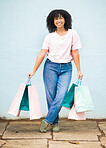 Shopping, retail and portrait of a woman with bags from a sale on a blue city wall in Greece. Fashion, product and girl shopper carrying content from a shop, boutique or store downtown with a smile