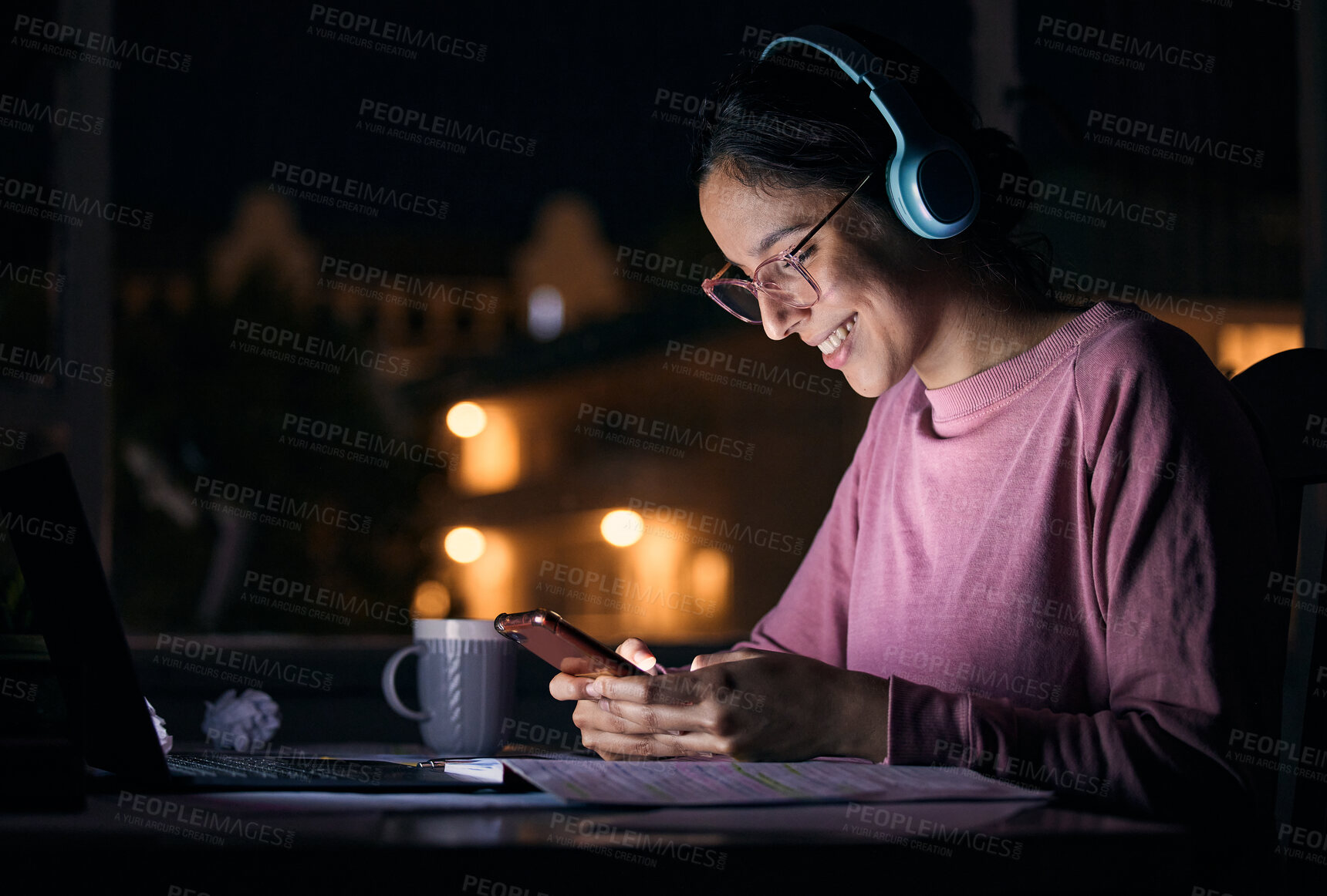Buy stock photo Phone, night and woman networking with headphones while listening to music, radio or podcast. Happy, smile and girl browsing social media, mobile app or internet with cellphone at a desk in her home.